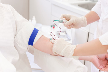 Doctor's hands take blood from a vein from a patient sitting in a chair. Blood test concept and...