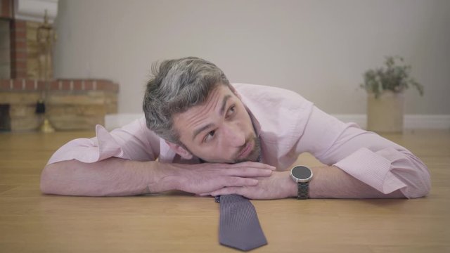 Portrait of henpecked husband or boyfriend laying on the floor. Beautiful female legs in red high-heel shoes passing by at the foreground. Sad handsome gray-haired Caucasian man controlled by spouse.