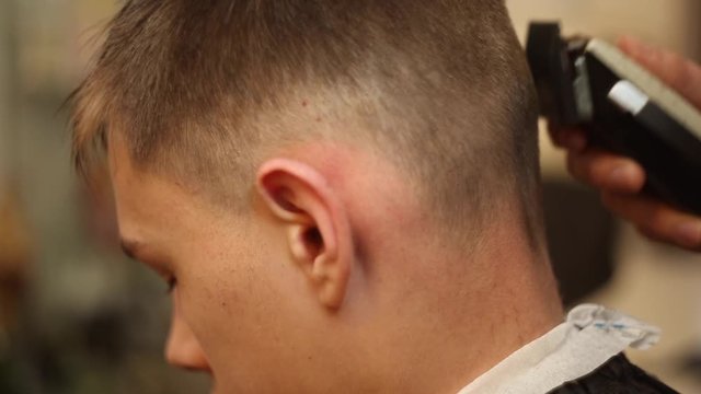 The hairdresser cuts the boy's hair clipper in the salon, making a stylish hairstyle.