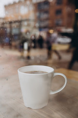Woman hand holding the cup of coffee or tea on rainy day window background in vintage color tone, copy space