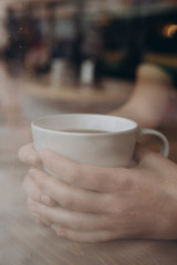 Woman hand holding the cup of coffee or tea on rainy day window background in vintage color tone, copy space