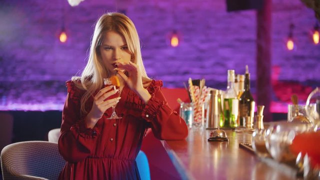 Gorgeous young woman sitting by the bartender stand - drinking a beverage from the straw