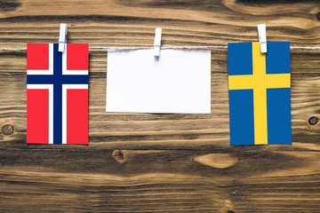 Hanging flags of Bouvet Islands and Sweden attached to rope with clothes pins with copy space on white note paper on wooden background.Diplomatic relations between countries.