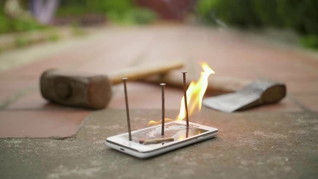 Broken with nails mobile phone on ground is on fire in slow motion