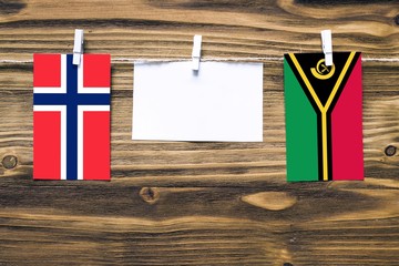 Hanging flags of Bouvet Islands and Vanuatu attached to rope with clothes pins with copy space on white note paper on wooden background.Diplomatic relations between countries.