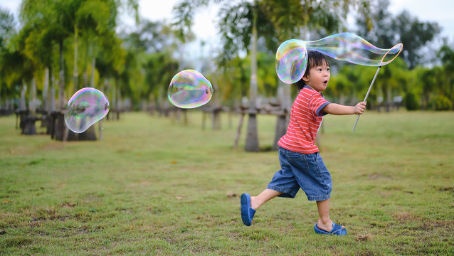 Cute Asian Kid making soap bubbles outside, summer time.