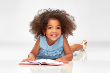childhood, school and education concept - happy smiling little african american girl reading book over grey background