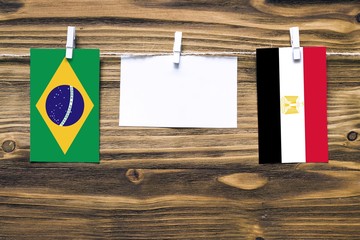 Hanging flags of Brazil and Egypt attached to rope with clothes pins with copy space on white note paper on wooden background.Diplomatic relations between countries.