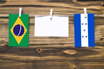 Hanging flags of Brazil and Honduras attached to rope with clothes pins with copy space on white note paper on wooden background.Diplomatic relations between countries.