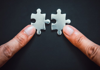 two fingers connect pieces of the silver metal puzzle on black color background with copy space,...