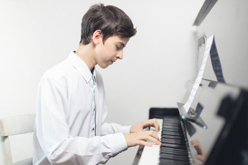 Naklejka na ściany i meble a teenage boy in a white shirt sits and plays the piano . a man plays a musical instrument piano