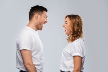 relationships, style and people concept - portrait of happy couple in white t-shirts looking at each and laughing other over grey background