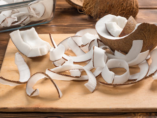 Close up view of dried coconut chips in on baking paper in a glass pan and on cutting board with coconut shells