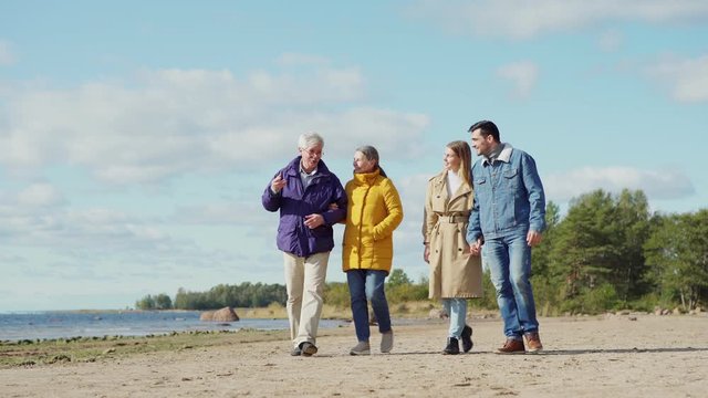 Wide shot of two happy loving couples, senior and young lovers, walking on sea shore together and talking joyfully on spring day