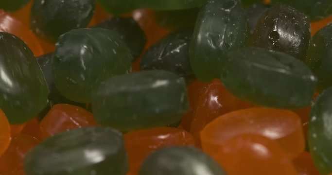 Green candies are poured into transparent bowl for orange sweets, closeup, abstract picture, two colors, lots of sweets, junk food, sweets, poor nutrition, preparation for Halloween, sweetness or muck