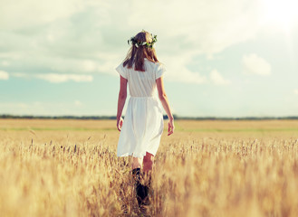 happiness, nature, summer holidays, vacation and people concept - smiling young woman in wreath of flowers and white dress walking along cereal field - Powered by Adobe