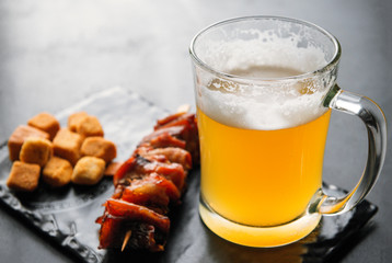 1 mug of light beer with foam with snacks on a dark background