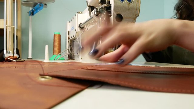 A seamstress sews a pocket to a leather bag in a sewing workshop. A woman operates sewing machine. Slave work concept 4k