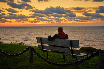 Woman sitting on bench at sunset over a lake