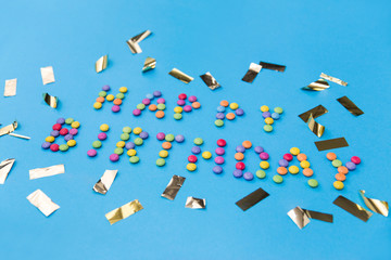 food, confectionery and sweets concept - happy birthday lettering made of candy drops and metallic confetti on blue background