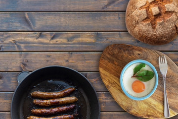 Pan-fried sausages and scrambled eggs served with bread on a wooden table, top view. free space for text