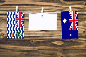 Hanging flags of British Indian Ocean Territory and Heard and Mcdonald Islands attached to rope with clothes pins with copy space on white note paper on wooden background.