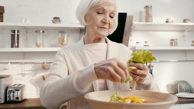 smiling woman adding lettuce to salad 