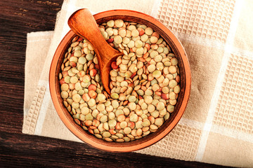 Lentils in a clay vessel and a wooden spoon on a napkin and wooden background