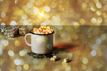 Obraz na płótnie Canvas White metal mug of cocoa or hot chocolate with marshmallows on a table with New Year's decor and sparkling bokeh lights in the background. Christmas house concept