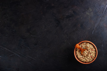 Fototapeta na wymiar Lentils in a clay vessel and a wooden spoon with place for text on a black concrete background