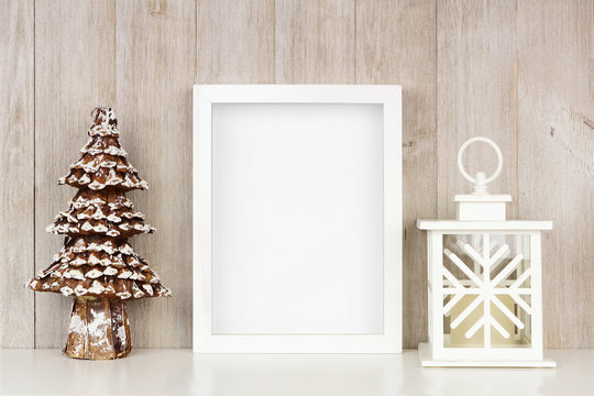 Mock up white frame with Christmas tree and lantern decor on a shelf. Portrait frame against a rustic gray wood wall.