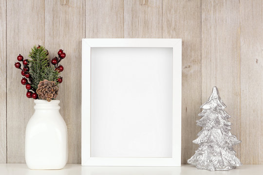 Mock up white frame with Christmas branches and silver tree on a shelf. Portrait frame against a rustic gray wood wall.