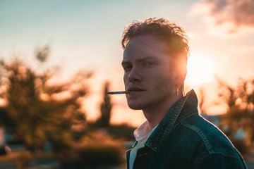 portrait of young man with 80s look smoking a cigarette during sunset