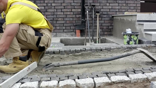 Residential Bricks Driveway Building. Caucasian Construction Worker Finishing Granite Decorative Brick Path.