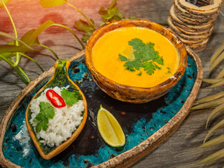 A plate of delicious pumpkin soup, a serving of rice with herbs and a slice of lime. On craft dishes