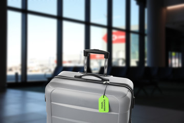 Grey suitcase with TRAVEL INSURANCE label in airport terminal