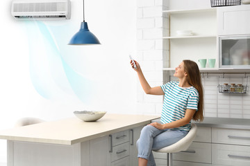 Young woman with air conditioner remote control at home