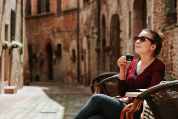 Young woman enjoying coffee in in a cafe in medieval town in Tuscany, Italy 