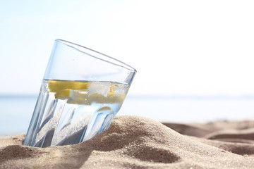 Sandy beach with glass of refreshing lemon drink on hot summer day, space for text