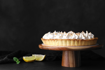 Stand with delicious lemon meringue pie on table against black background