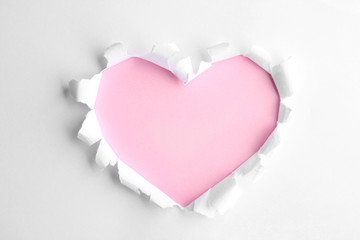 Torn heart shaped hole in white paper, top view. Pink space for text
