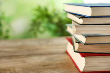 Stack of hardcover books on wooden table against blurred background, closeup. Space for text