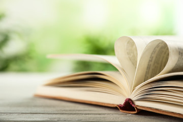 Heart made of book pages on wooden table against blurred background, closeup. Space for text