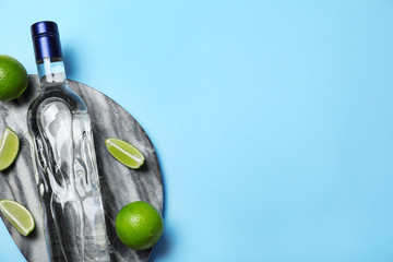 Bottle of vodka and limes on light blue background, top view. Space for text