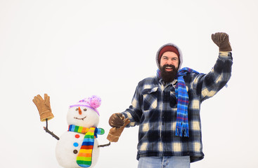 Man in winter clothes standing near snowman. Bearded man holds snowman by hand. Wintertime. Winter fashion. Snowman in hat, scarf, gloves. Happy holiday. Bearded man with snowman. Christmas snow man.