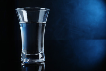 Shot glass of vodka on dark background with blue light. Space for text