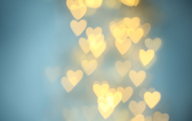 Blurred view of beautiful gold heart shaped lights on light blue background