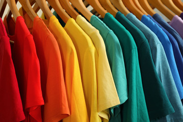 Hangers with bright clothes as background, closeup. Rainbow colors