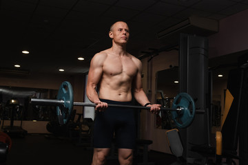 Fototapeta na wymiar Muscular bodybuilder guy doing exercises with barbell in gym. Brutal strong athletic man pumping up muscles and train in gym workout.