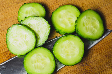 Cucumber slices and knife on a wooden board. vegetable slicing process. cooking food